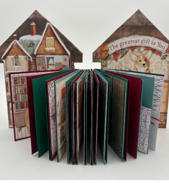 Album maison de Noël ouvert en éventail, pages rouges et vertes et chalets enneigés