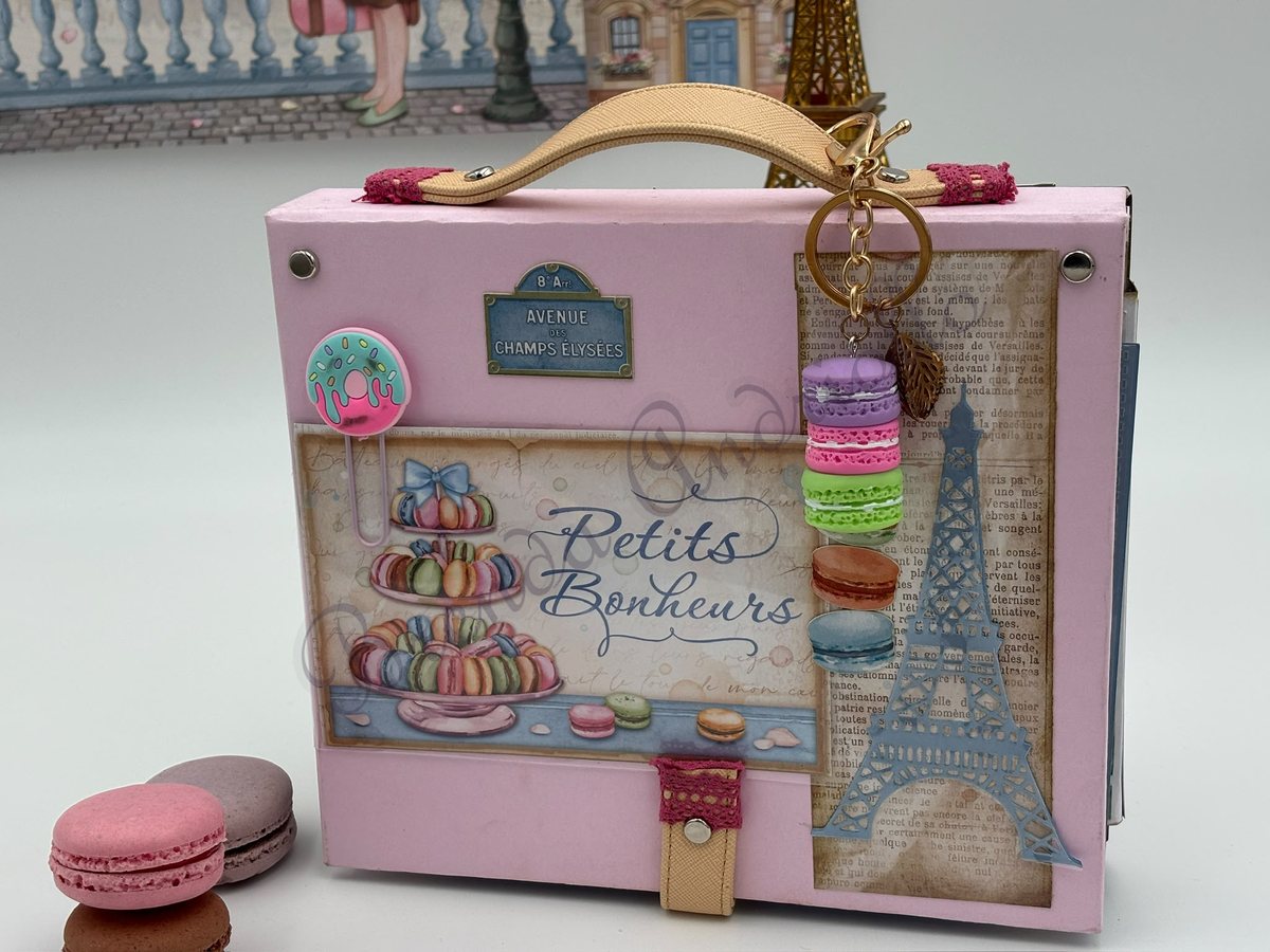 Valisette « Petits Bonheurs » debout, Tour Eiffel et macarons en papier, devant un décor parisien
